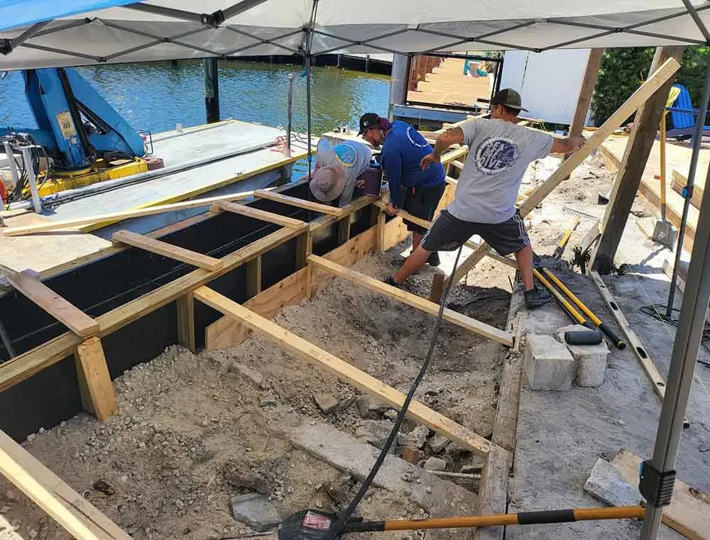 Crew working on modern seawall repair using wood formwork and reinforcement materials along the shoreline