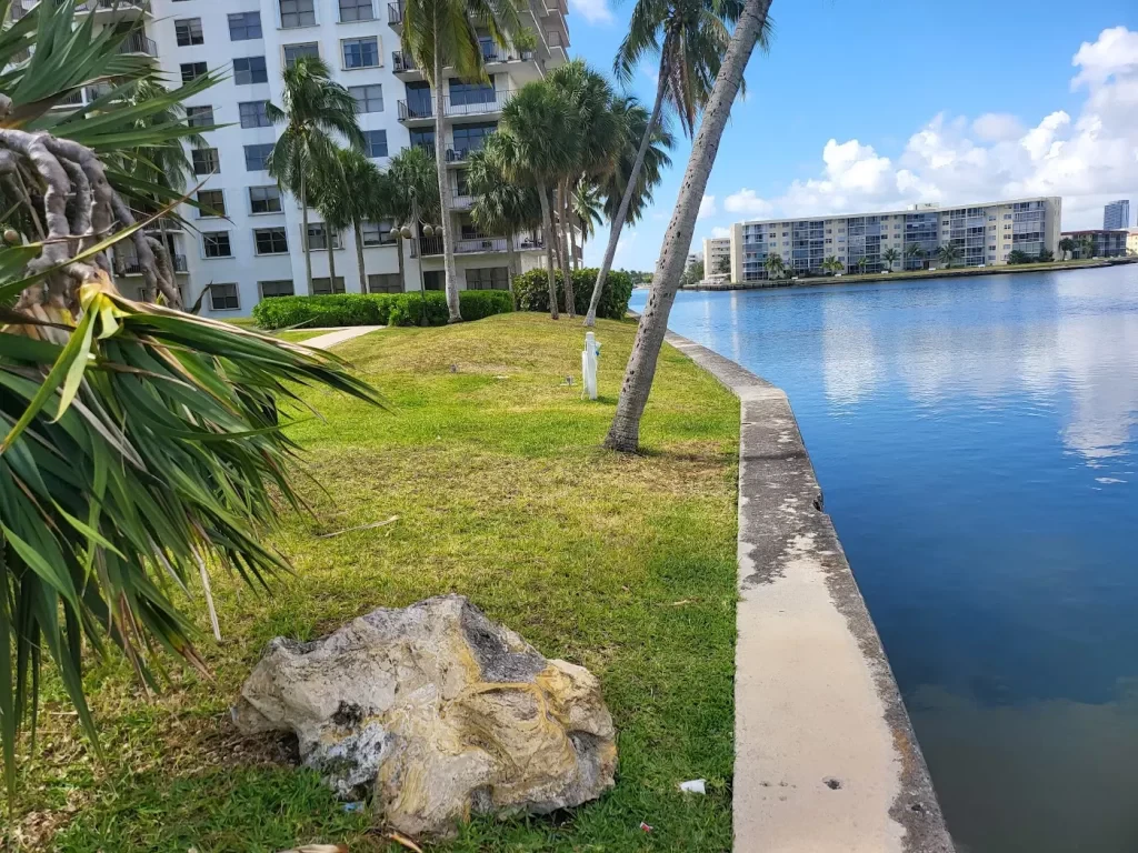 Waterfront apartment complex with palm trees and a lake on a sunny day.