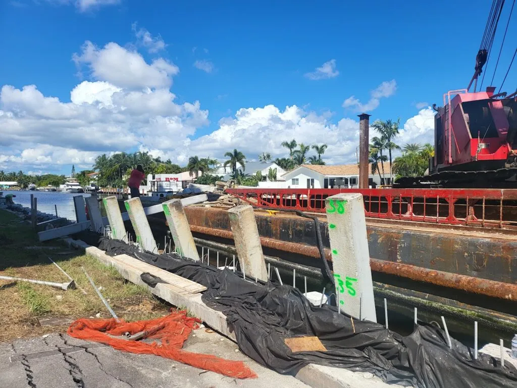 Concrete seawall construction in progress along a waterfront with steel reinforcements and heavy equipment.